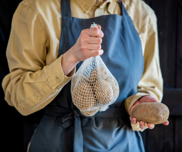 Female in apron holds potatoes in basket